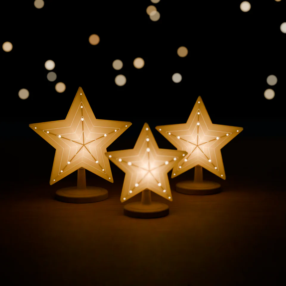Drei weiße facettierte Lichtsterne auf Steckständern, von innen warm beleuchtet, auf einem Holztisch vor dunklem Hintergrund